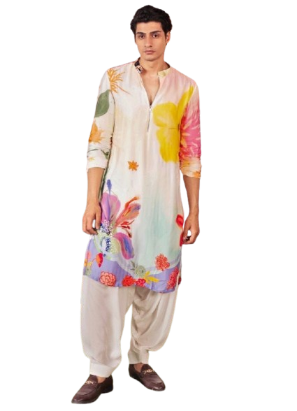 Man wearing colorful floral-printed traditional tunic with white pants in decorated setting.